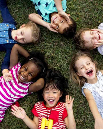 a circle of kids lay on the grass, smiling and laughing